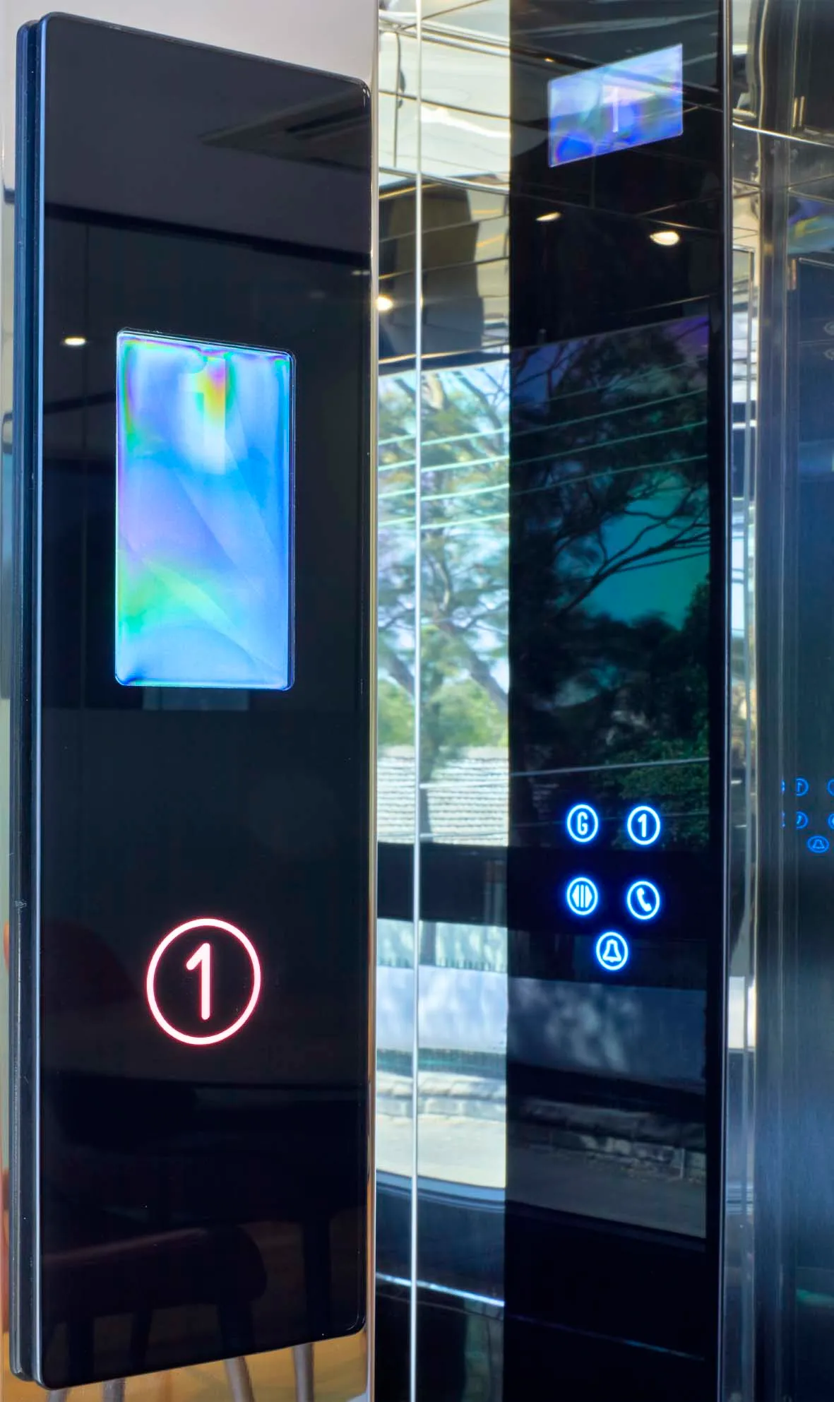 Nærbilde av betjeningspanel i sort glass med opplyste etasjeknapper på heis med speilfront
