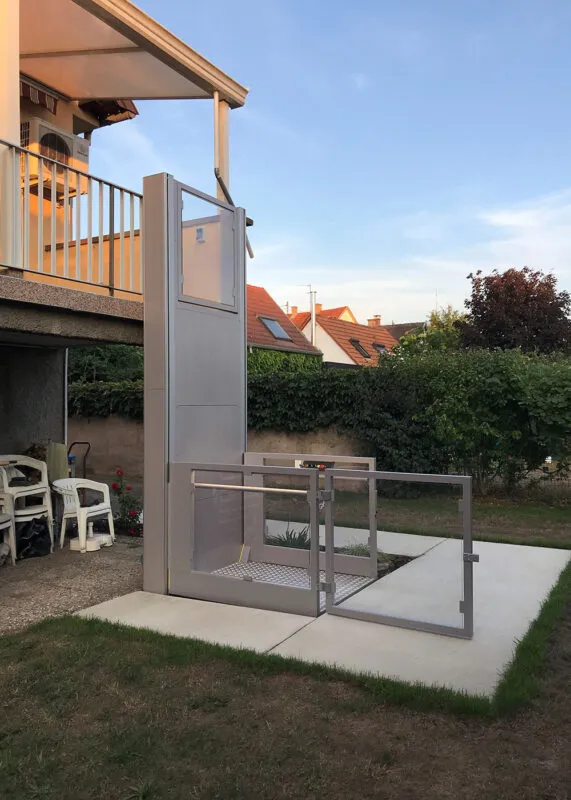 Utvendig løfteplattform i grått med port og glassvegger ved terrasse på bolig